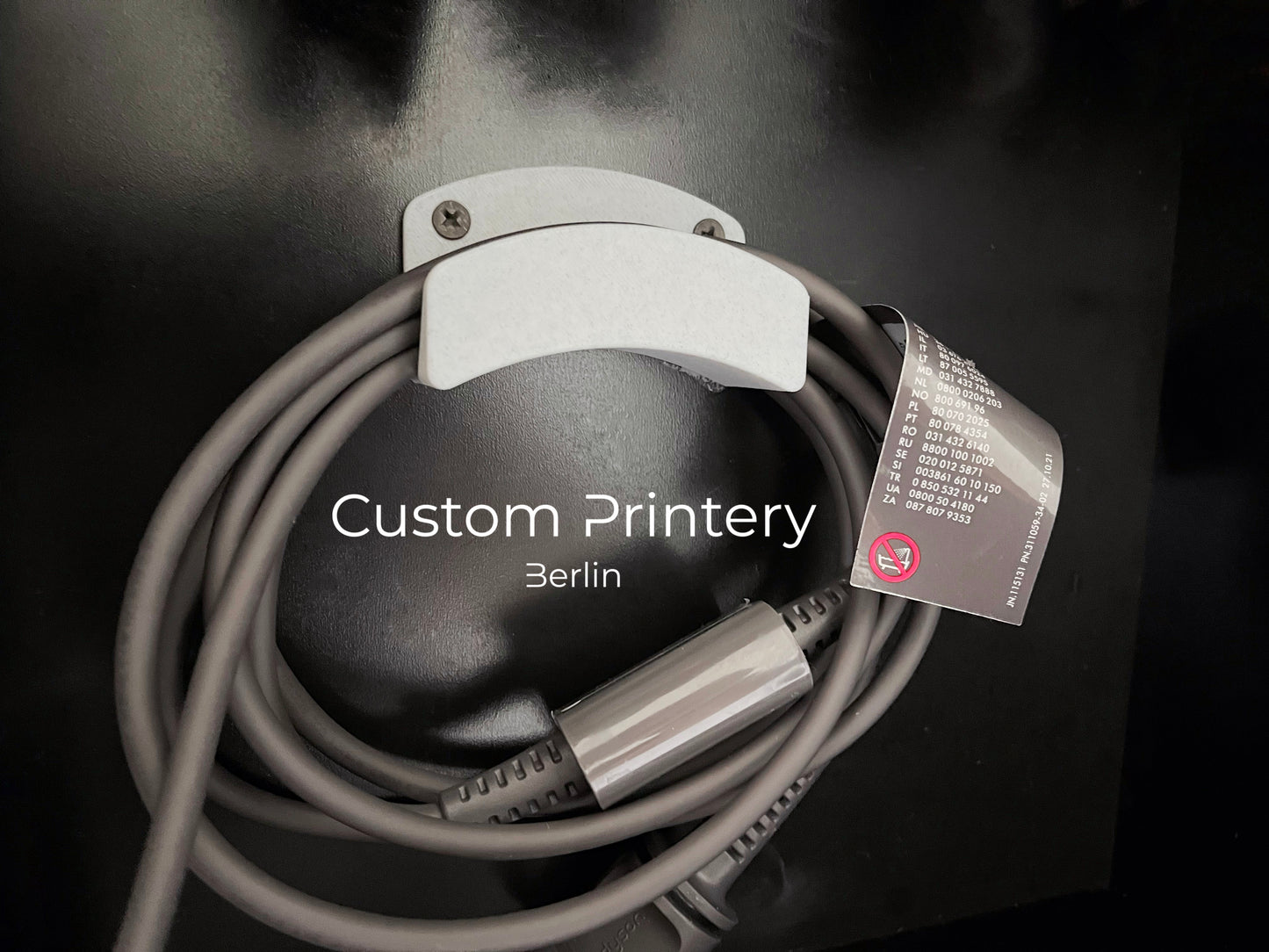 Schwarze Wandhalterung für Dyson Haarstyling-Gerät und Zubehör. Die Halterung enthält den Haartrockner, verschiedene Styling-Aufsätze und ist sauber organisiert. Oben auf dem Regal steht eine moderne Vase mit getrockneten Eukalyptuszweigen.