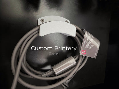 Schwarze Wandhalterung für Dyson Haarstyling-Gerät und Zubehör. Die Halterung enthält den Haartrockner, verschiedene Styling-Aufsätze und ist sauber organisiert. Oben auf dem Regal steht eine moderne Vase mit getrockneten Eukalyptuszweigen.