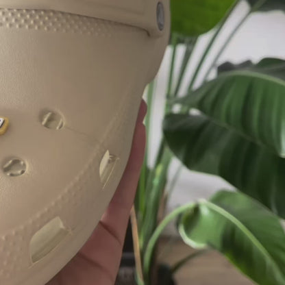 Custom black Crocs with colorful personalized name charms for 'Lena,' 'Noah,' 'Theo,' and 'Clara' from Custom Printery Berlin, showcased in a casual indoor setting with green plants.